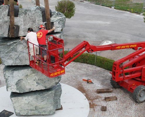 Rachbauer GmbH - Straßwalchen - Salzburg - Ihr starker Partner! - Diesel Gelenkarbeitsbühne hilft beim Aufstellen von einer Steinskulptur von Herrn Weyringer